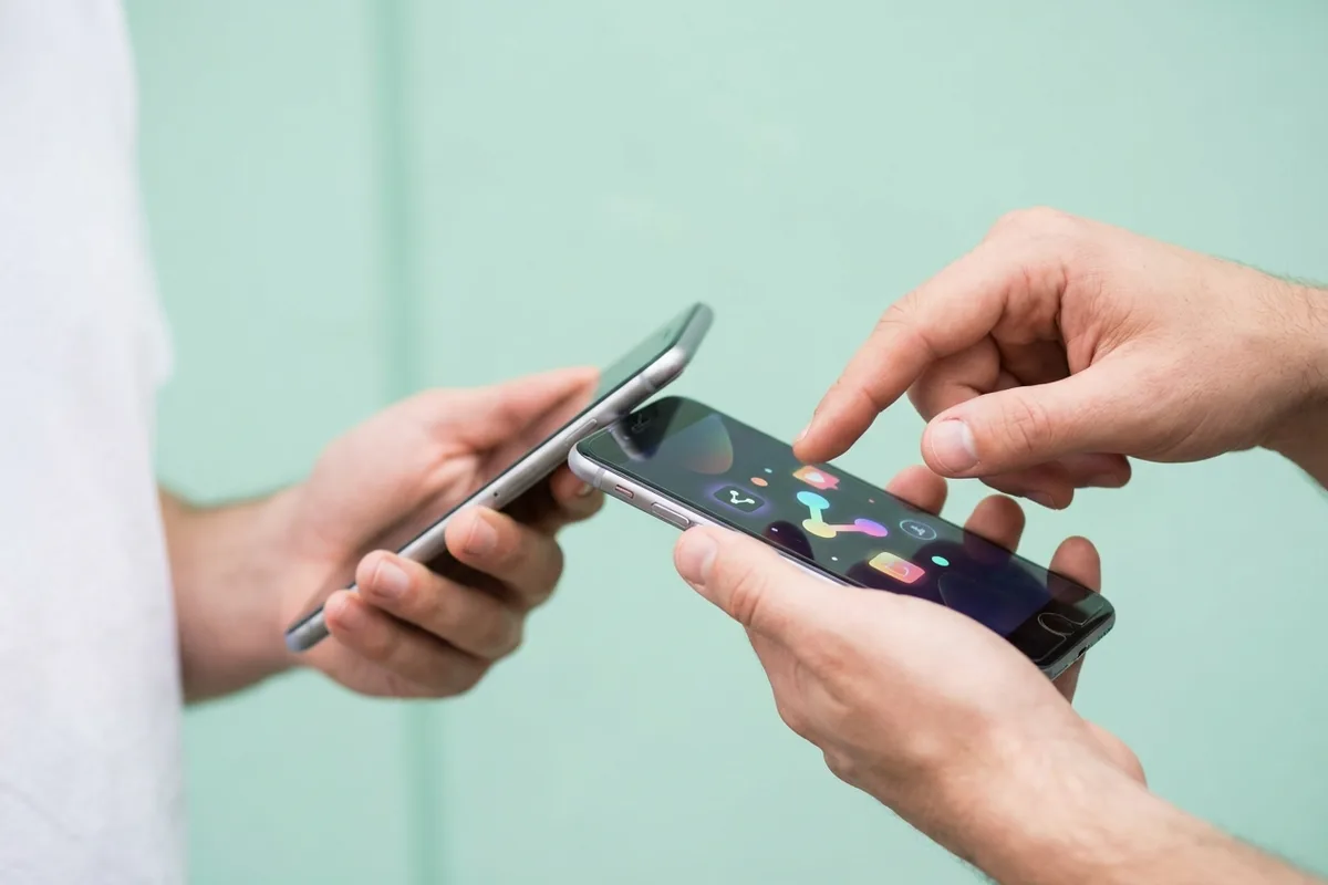 Two people holding phones side by side, one about to tap the other's share button